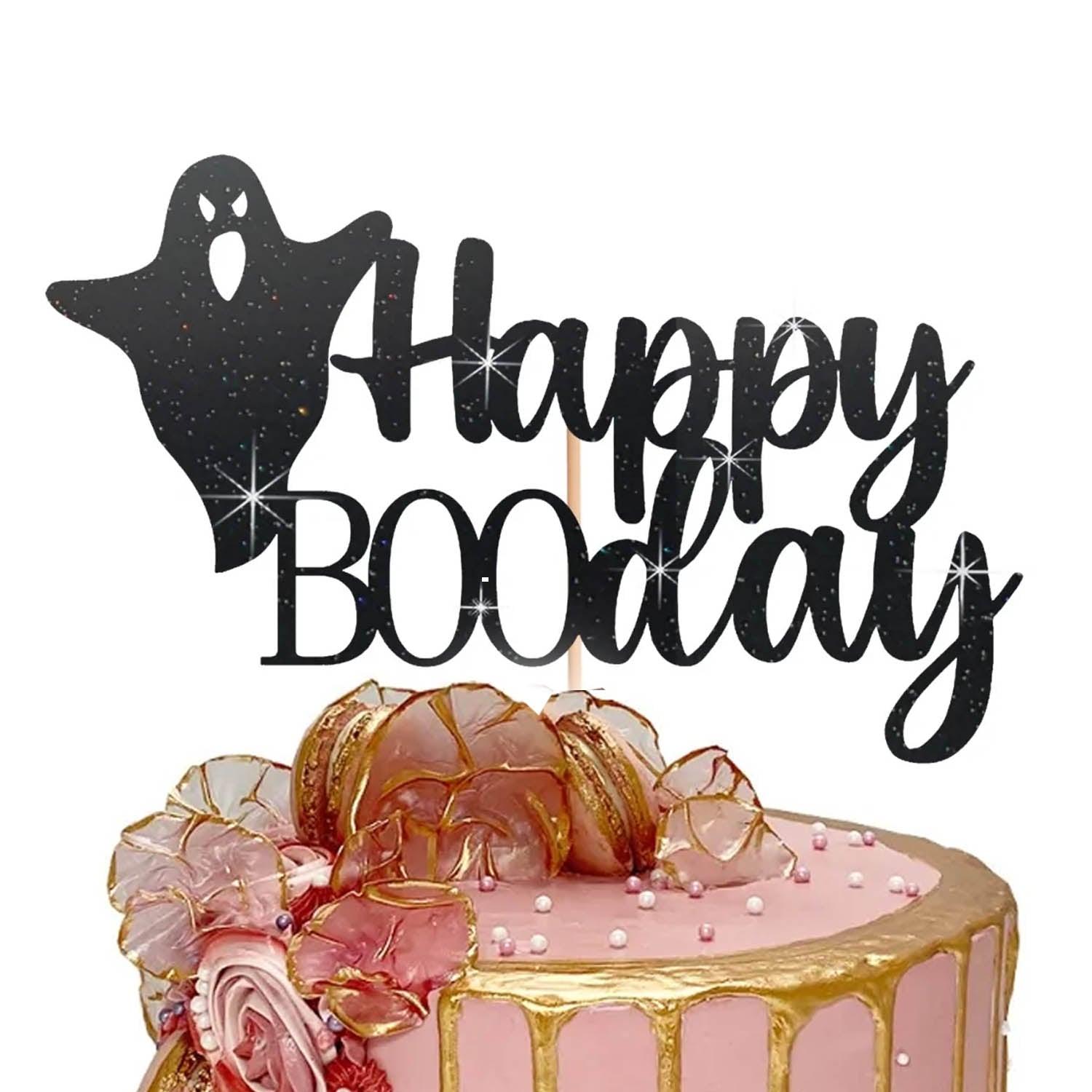 Pink birthday cake with gold drip, pink edible flowers, macarons, and a black glittery Happy Boo Day ghost topper.