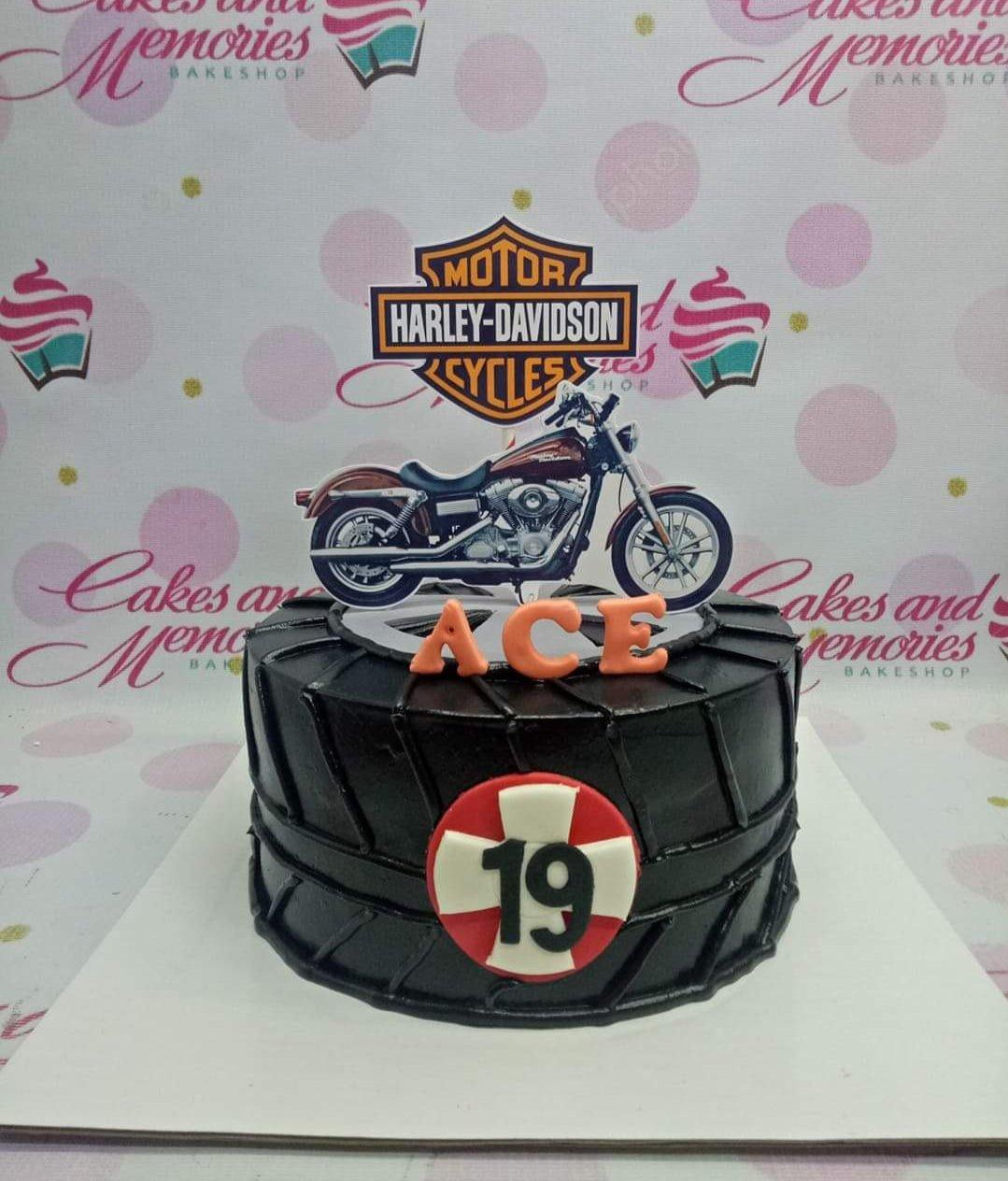 Black tire-themed Harley-Davidson cake with motorcycle printout topper and orange Ace name letters.