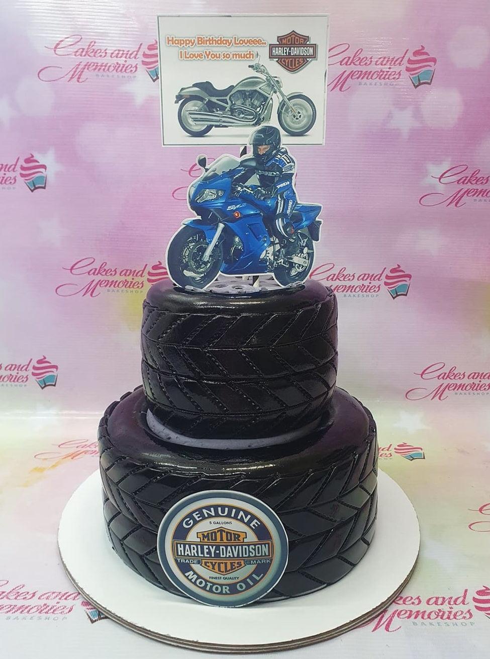 Two-tier black tire-themed Harley Davidson cake with motorcycle toppers and a logo on the front.