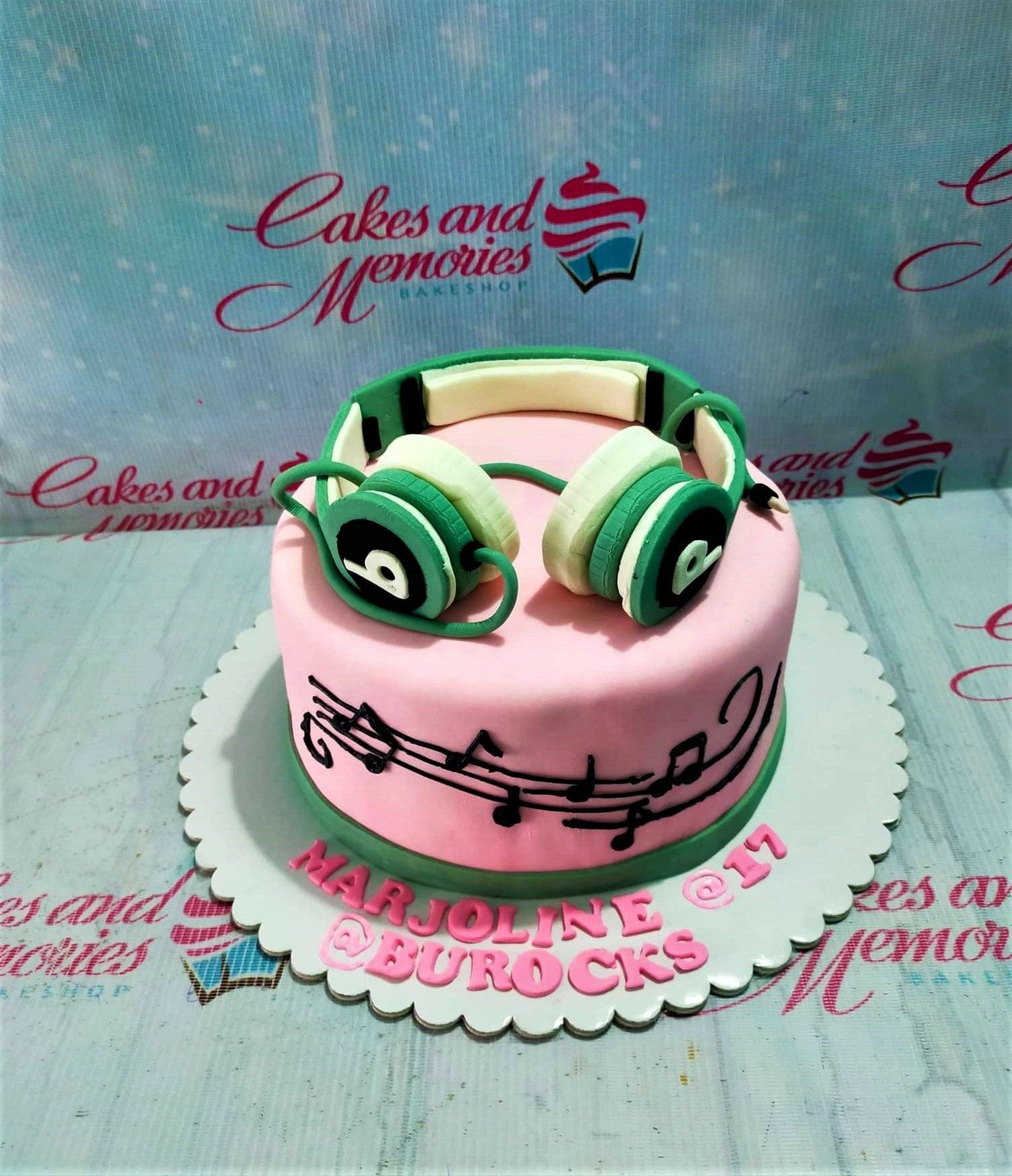 Pink fondant cake with green 3D headphones and black musical notes on the side.