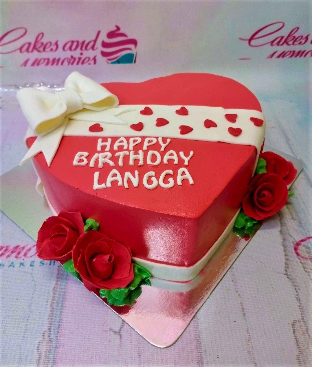 Red heart-shaped birthday cake with a white fondant bow, red heart accents, and red icing roses.
