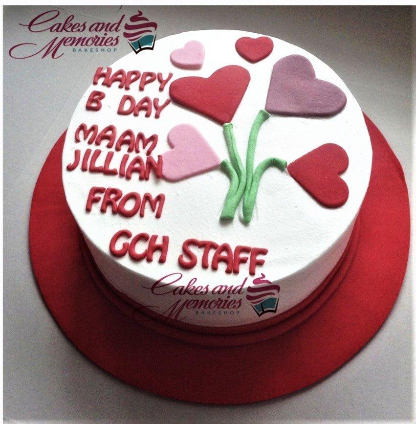 White round cake with red icing text and colorful fondant hearts on green stems.