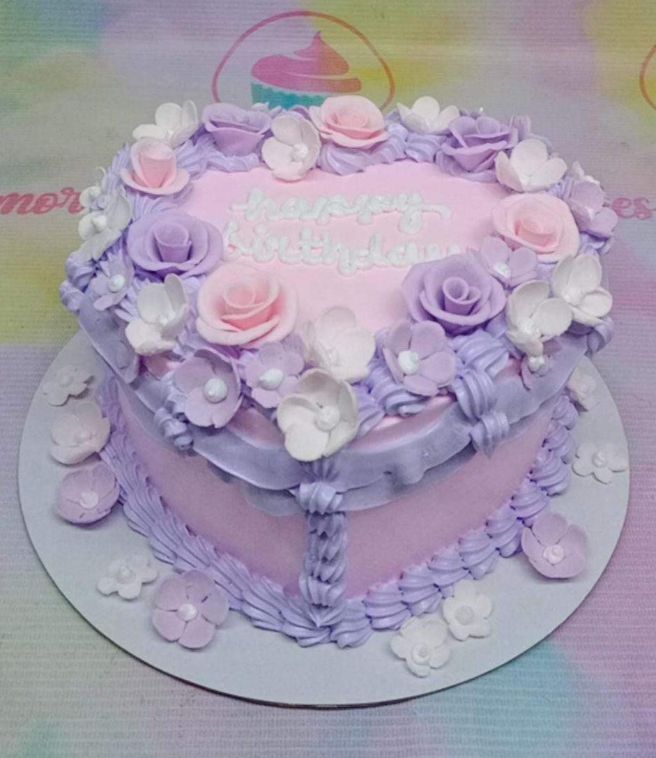 Heart-shaped pink birthday cake with purple and pink icing roses and white flowers