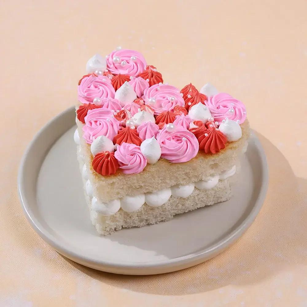 Heart shaped bento cake with pink and red icing rosettes and white cream dollops topped with white pearls.