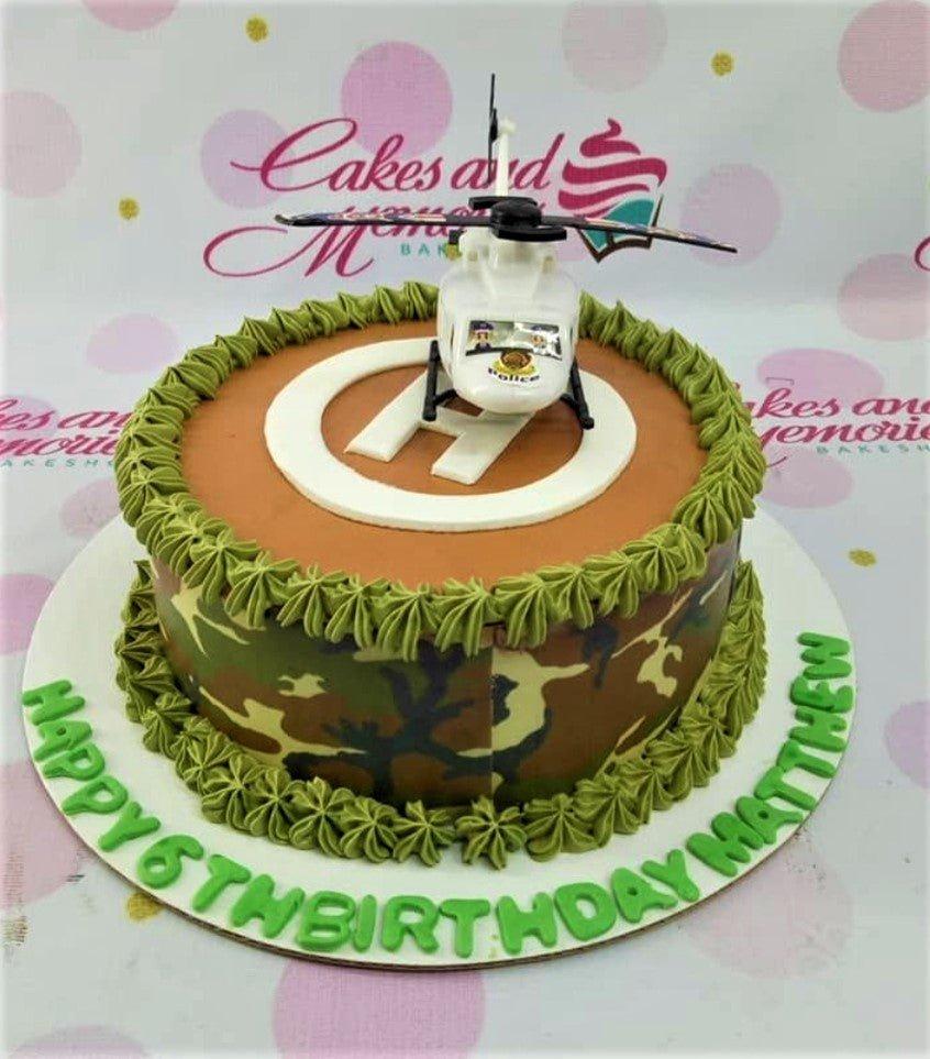 Camouflage themed birthday cake with a white police helicopter toy topper and green icing borders.