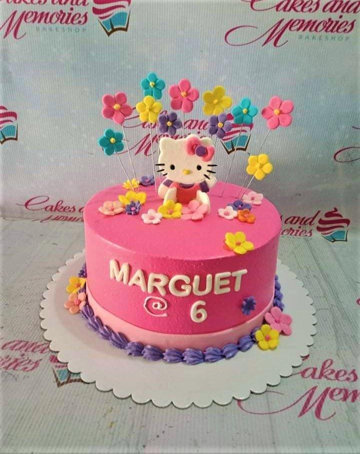 Pink Hello Kitty birthday cake with colorful fondant flowers on wires and a purple piped border.