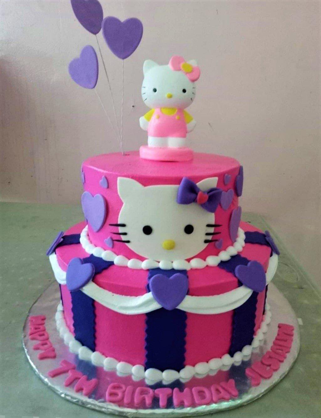 Two-tier pink and purple Hello Kitty birthday cake with heart decorations and a 3D character topper.