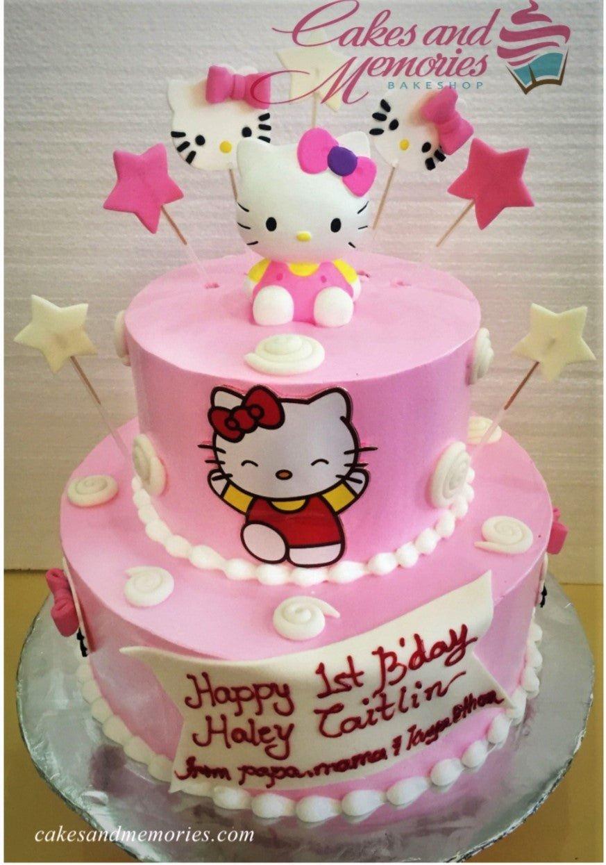 Two-tier pink Hello Kitty birthday cake with a 3D fondant figure, printed character toppers, and white icing swirls.