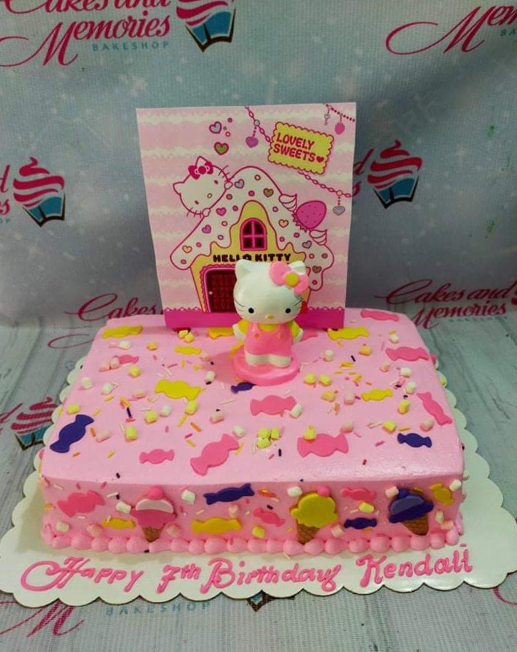 Pink rectangle Hello Kitty birthday cake with candy-shaped fondant decorations and a large Hello Kitty house backdrop.