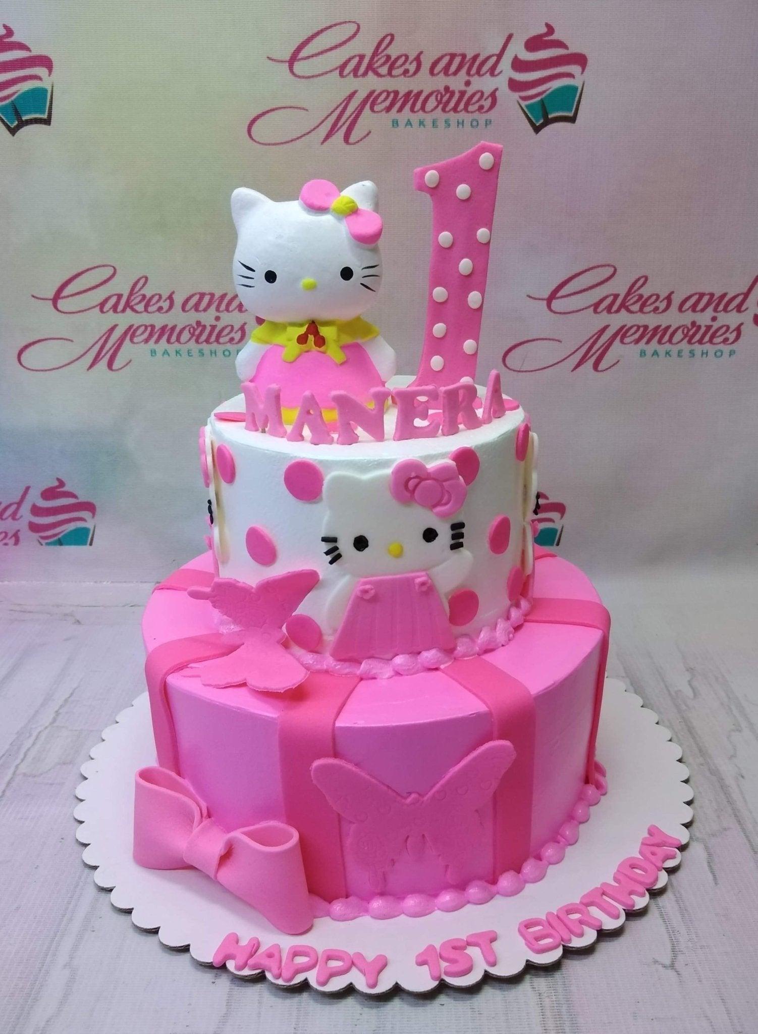 Two-tier pink and white Hello Kitty themed birthday cake with fondant butterflies, bows, and a 3D Hello Kitty topper.