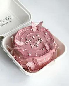 Pink bento cake with textured soft icing, edible butterfly toppers, and white piped message 'she's a hijabi' in a white takeout box.