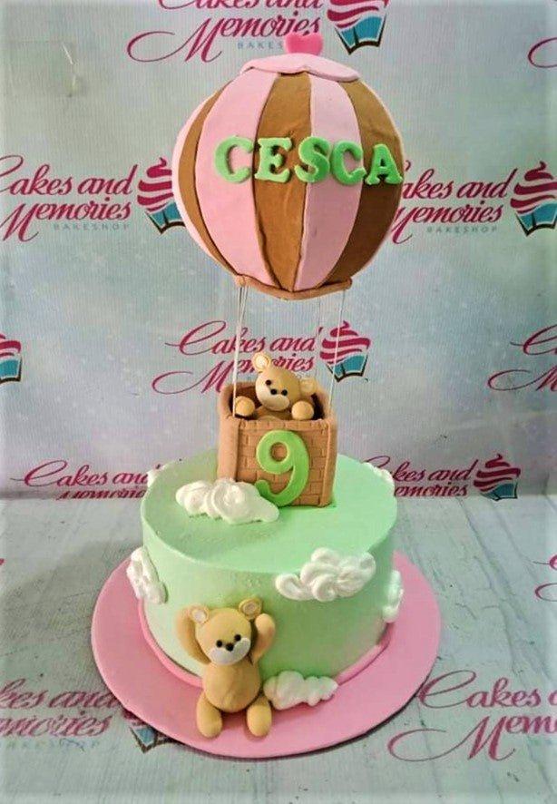 Light green hot air balloon cake with fondant bears, white clouds, and a pink base board.