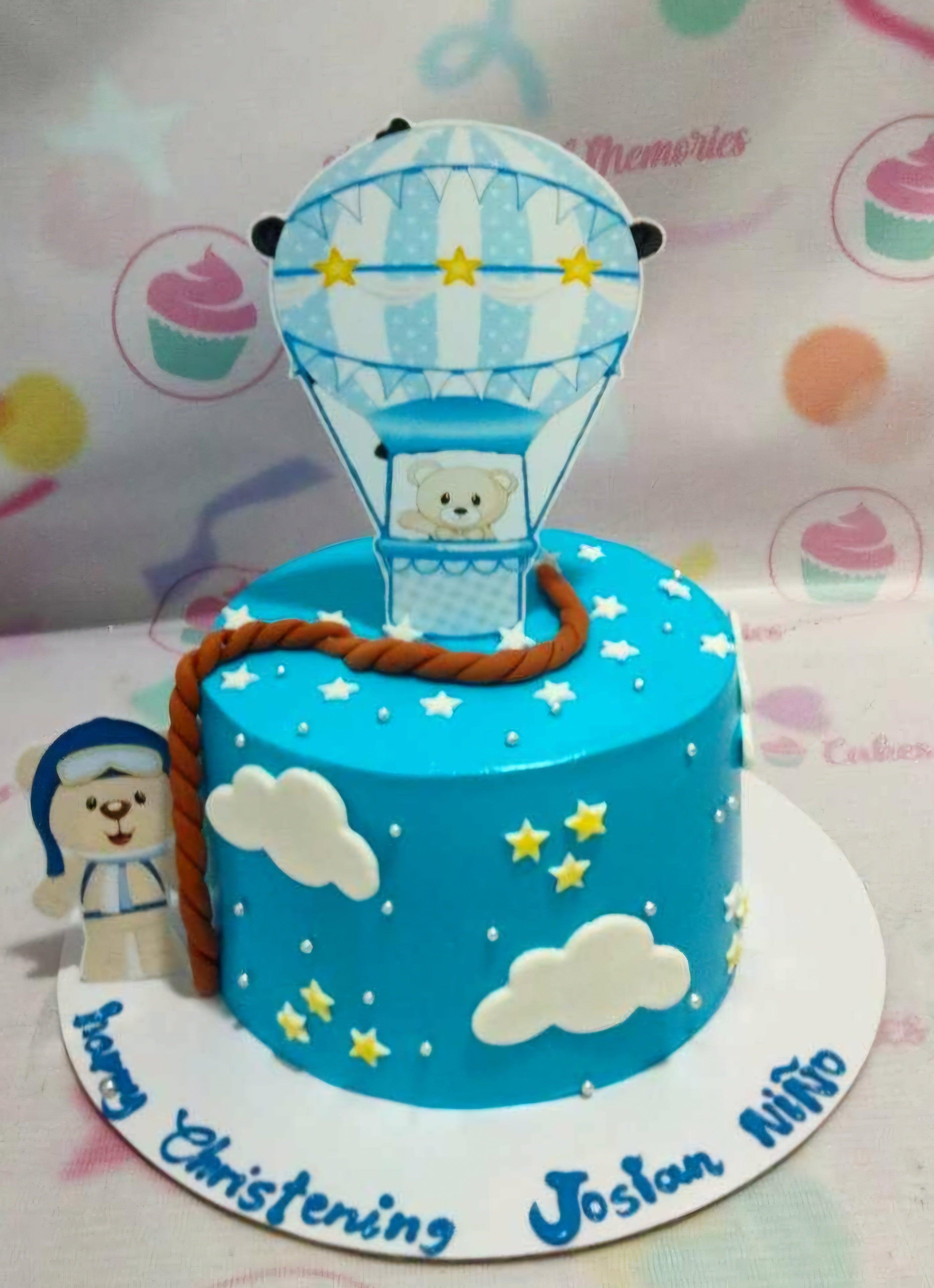 Blue hot air balloon christening cake with teddy bear toppers, white clouds, and yellow stars on a blue icing base.