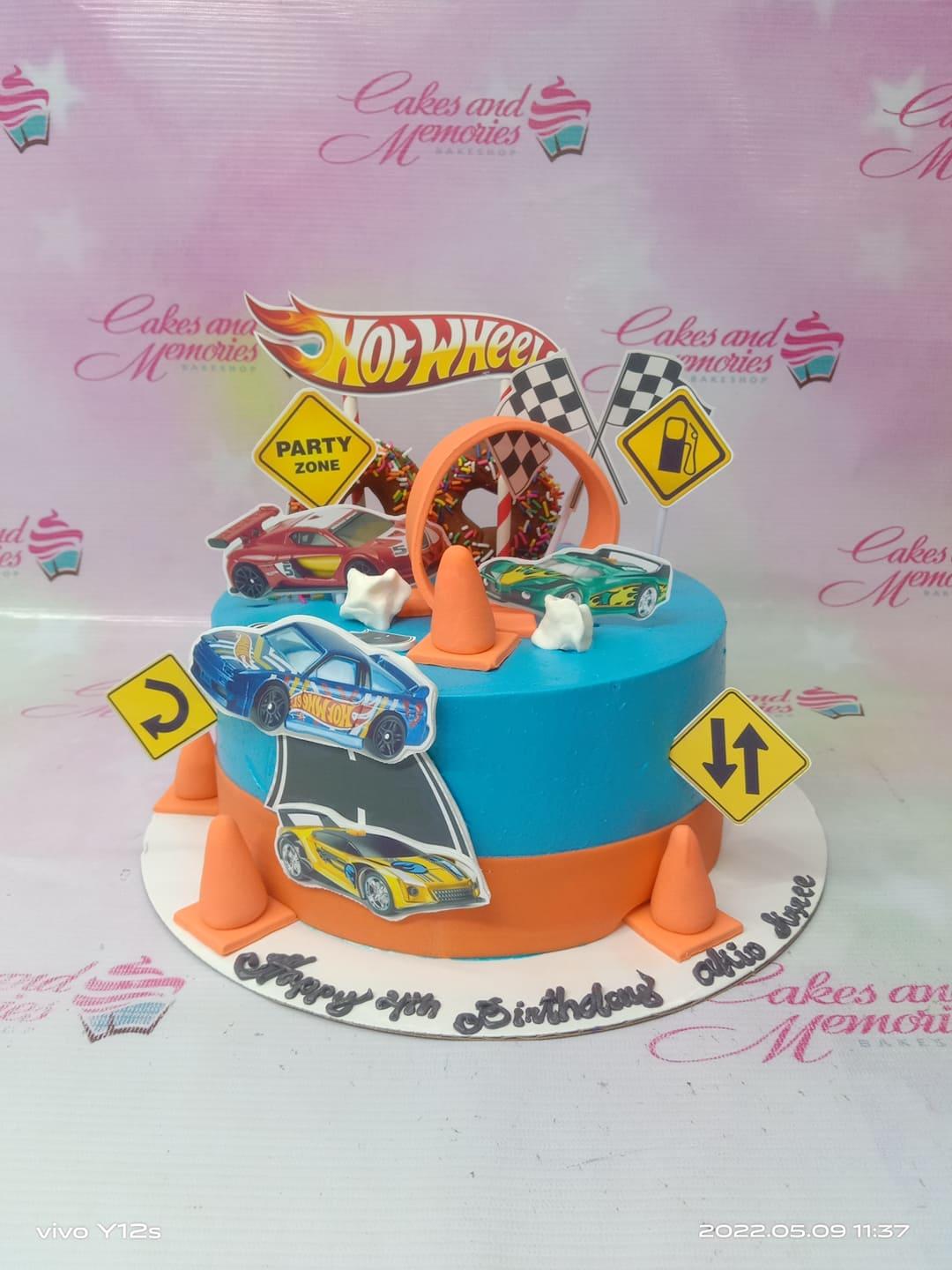 Hot Wheels themed birthday cake with blue and orange icing, toy cars, traffic signs, and a loop-the-loop topper.