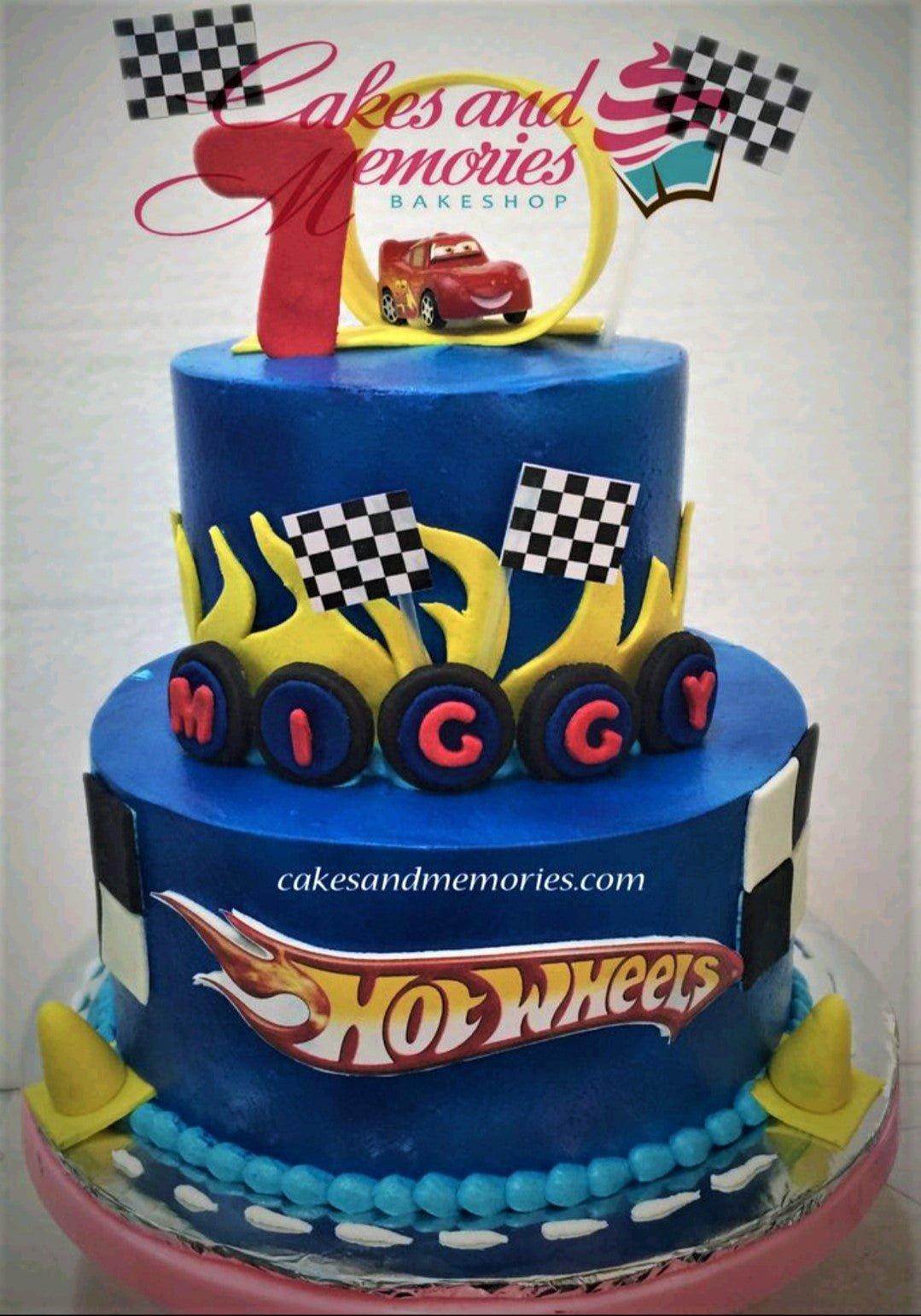 Two-tier blue Hot Wheels and Cars themed birthday cake with Lightning McQueen topper, checkered flags, and yellow flames.