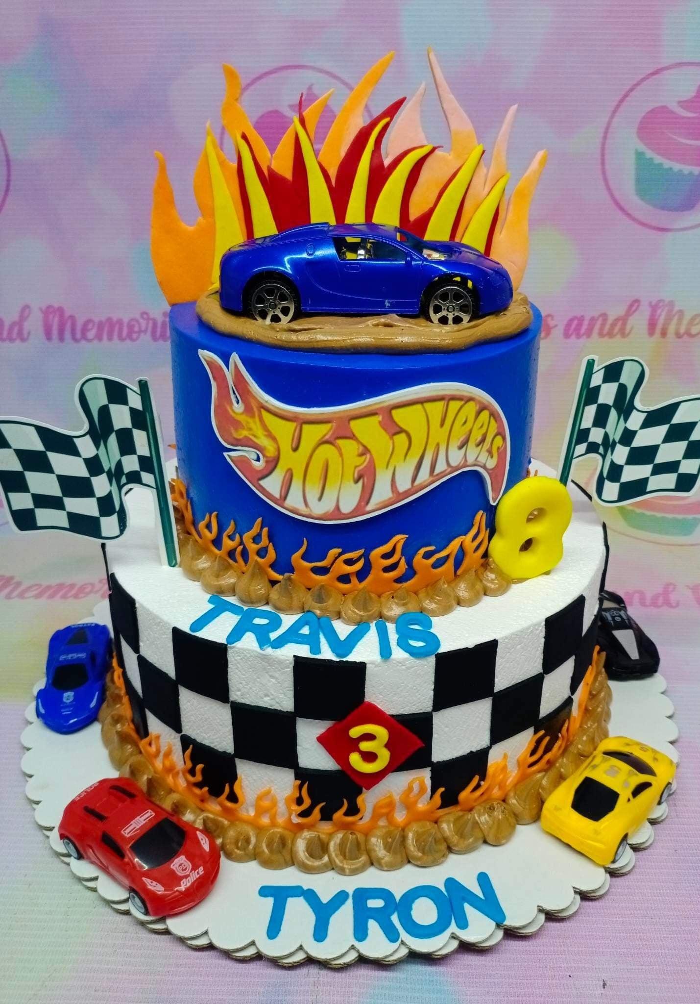 Two-tier Hot Wheels themed birthday cake with a blue top tier, checkered bottom tier, toy cars, and fondant flames.