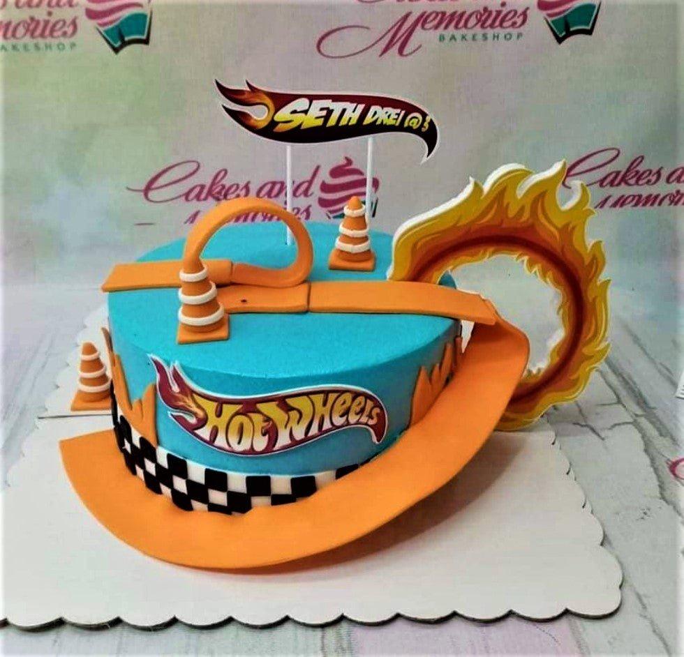 Hot Wheels themed blue birthday cake with orange racing track, checkered flag pattern, and flame toppers.