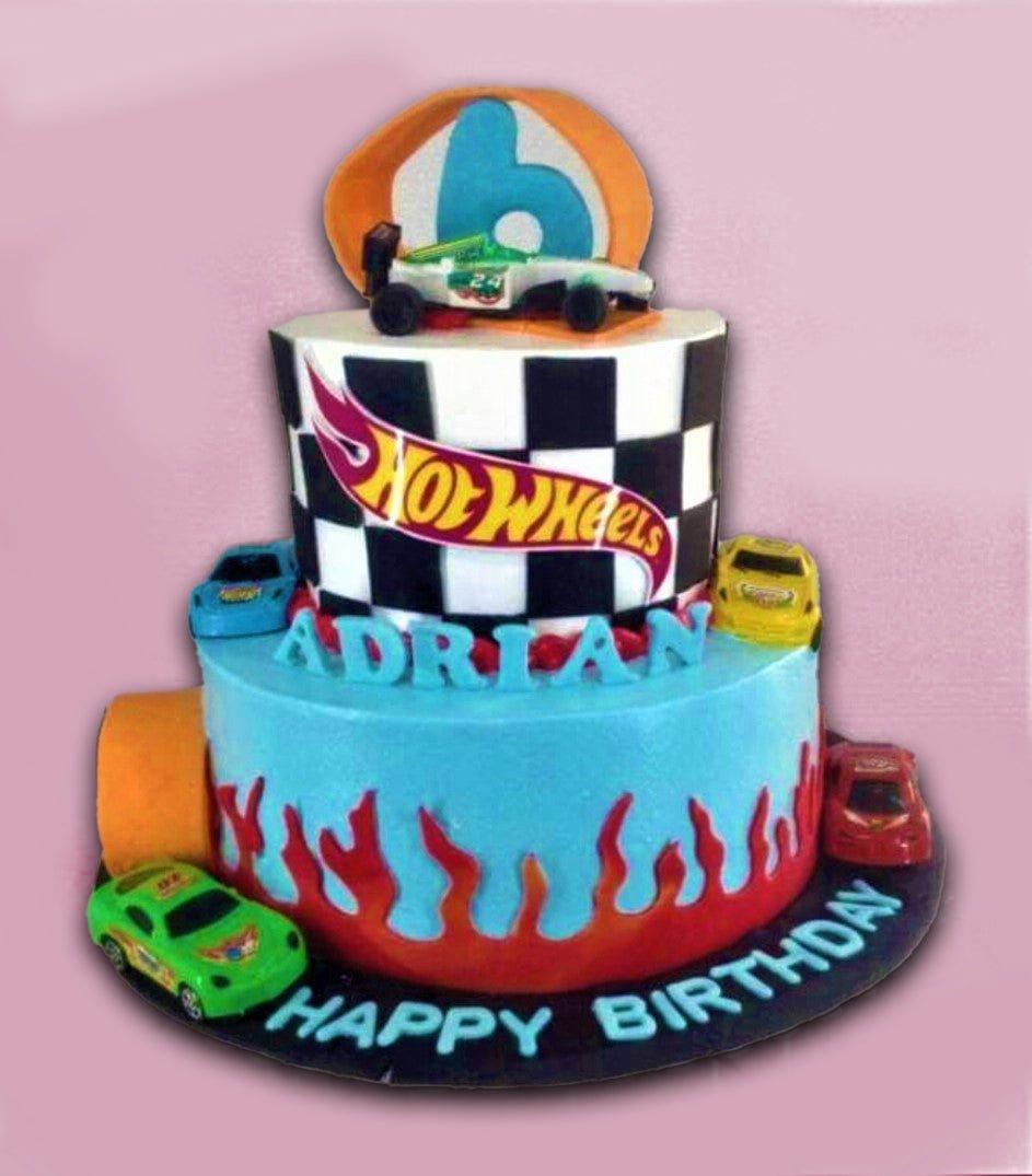 Two-tier Hot Wheels themed birthday cake with checkered top tier, blue bottom tier with red flames, and toy car toppers.