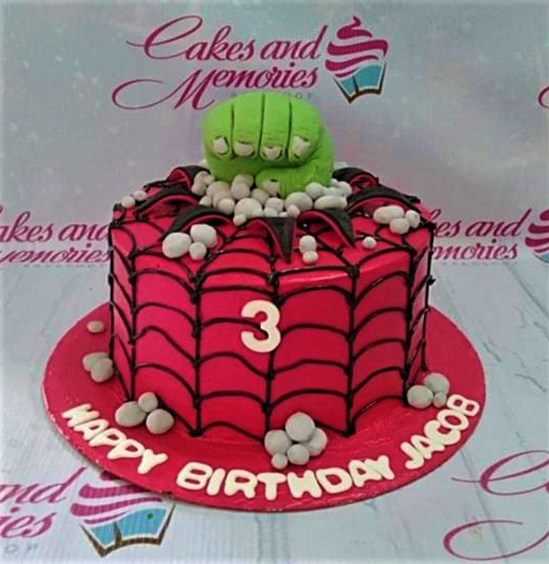 Red Spiderman and Hulk themed birthday cake with black spiderweb icing and a green fist topper.