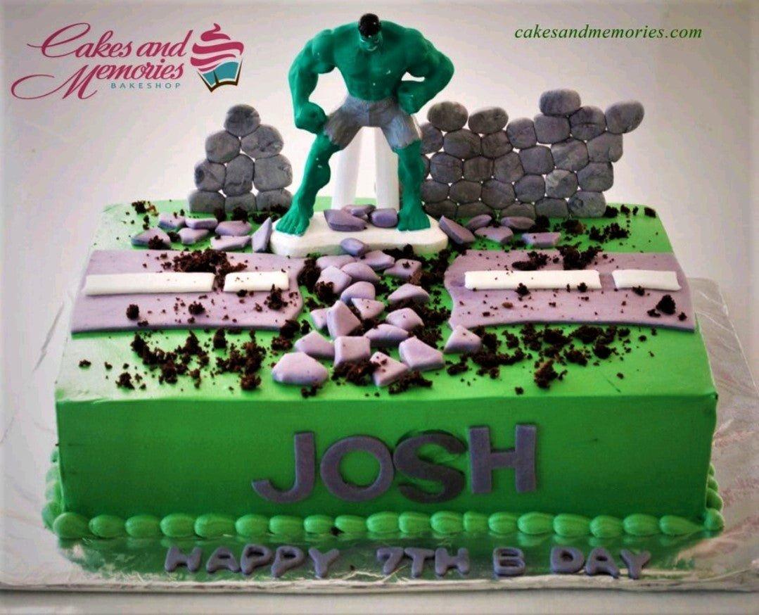 Green Hulk themed rectangle cake with a 3D Hulk figure smashing through a purple road and stone wall decorations.