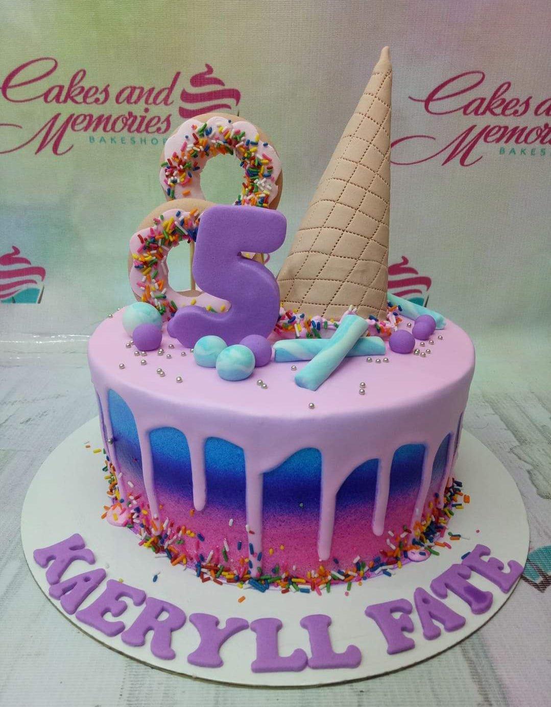 Pink and blue gradient cake with a large purple number 5, ice cream cone, and donut toppers with colorful sprinkles.