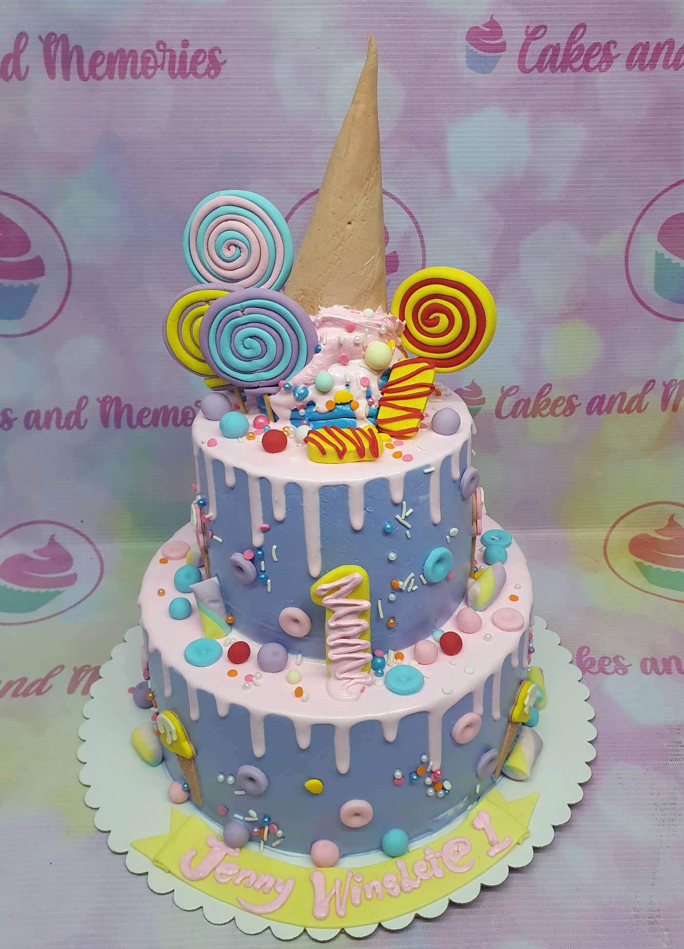 Two-tier purple ice cream themed cake with pink drip, lollipops, and an upside-down ice cream cone topper.