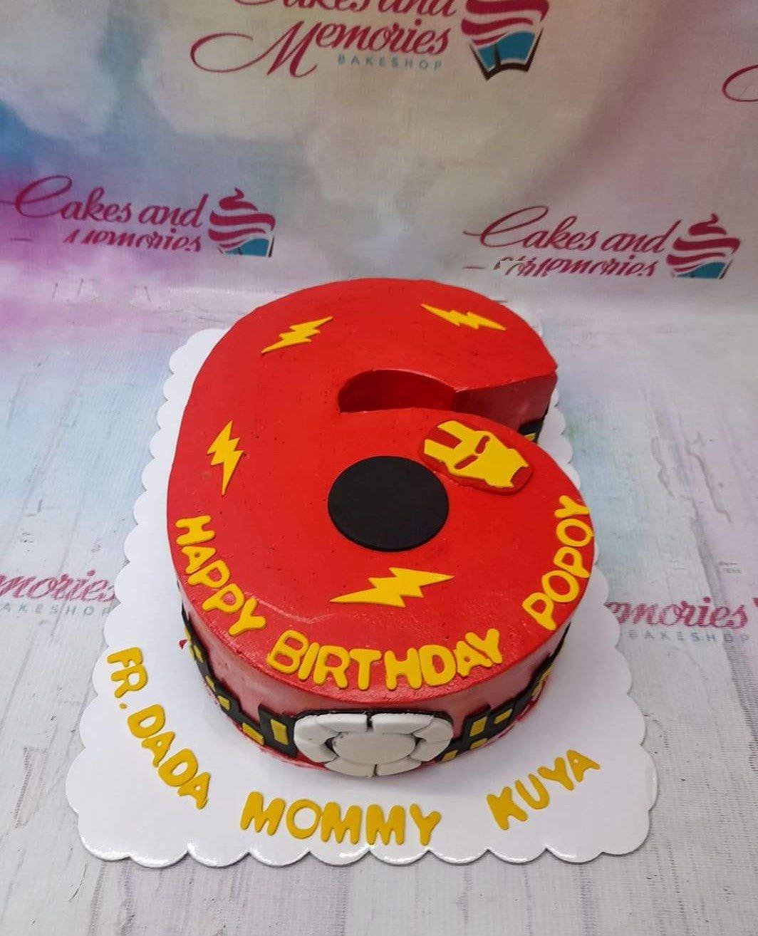 Red number 6 shaped cake with yellow lightning bolts and Iron Man themed decorations for a birthday celebration.