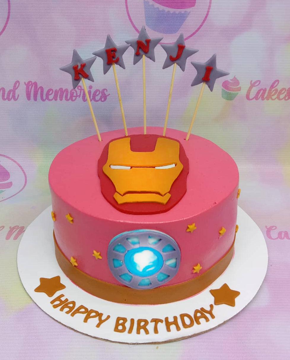 Pink Iron Man themed birthday cake with a fondant mask on top and an arc reactor on the side, featuring star toppers spelling Kenji.