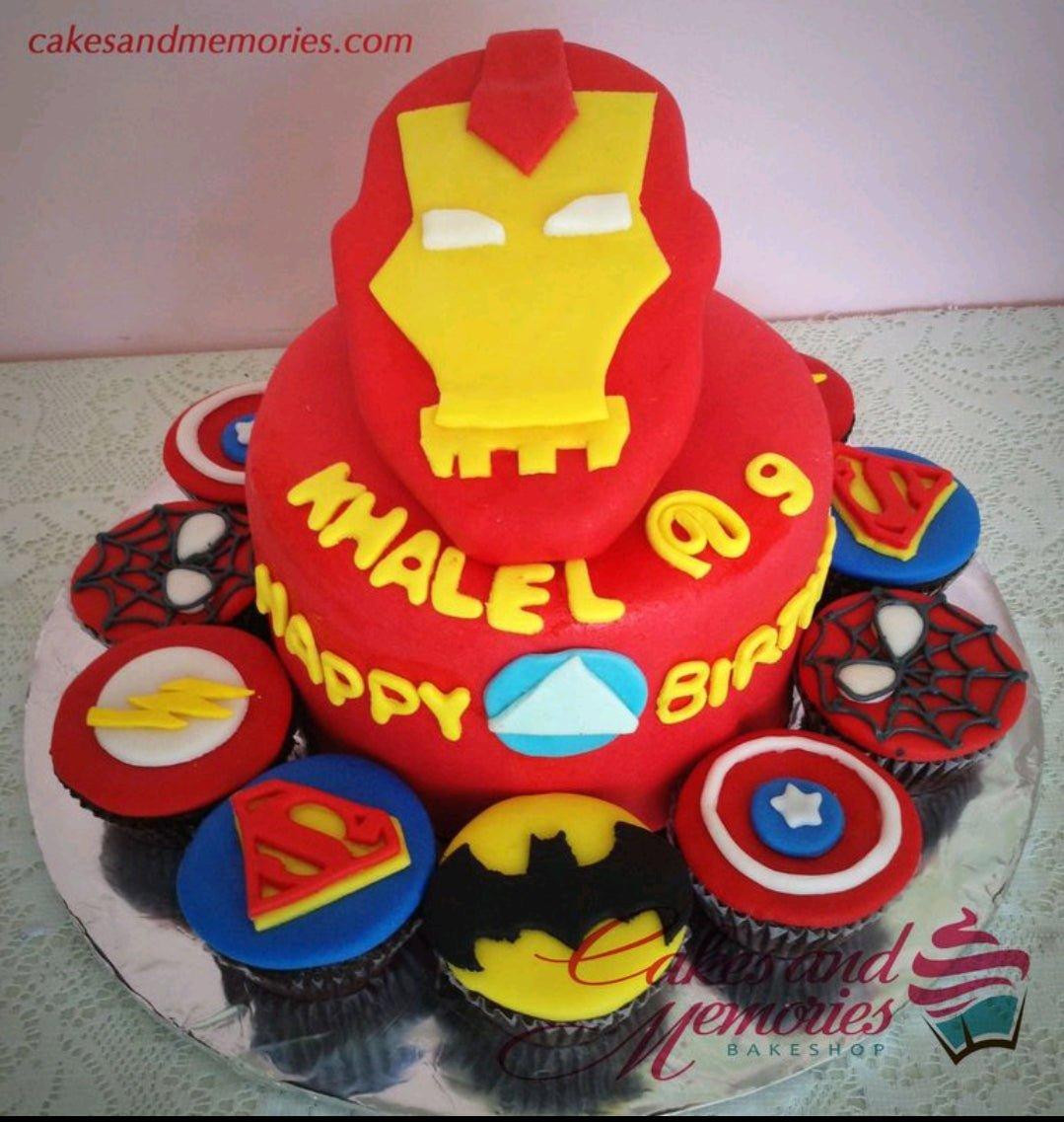 Red Iron Man themed fondant cake with superhero logo cupcakes featuring Spiderman, Batman, Superman, and Captain America.
