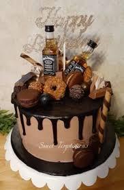 Chocolate drip cake with Jack Daniel's mini bottles, macarons, chocolates, and a silver glitter Happy Birthday topper.