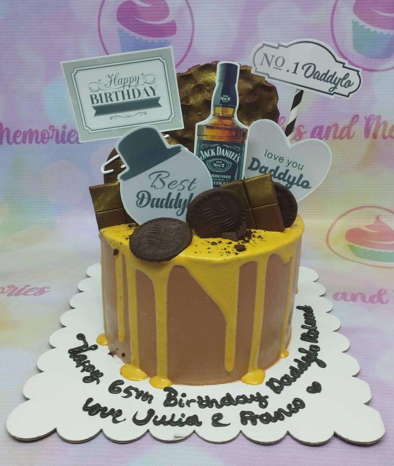 Brown 1-tier birthday cake with yellow drip, Jack Daniel's printout, chocolate bars, and Oreo cookies for a 65th birthday.