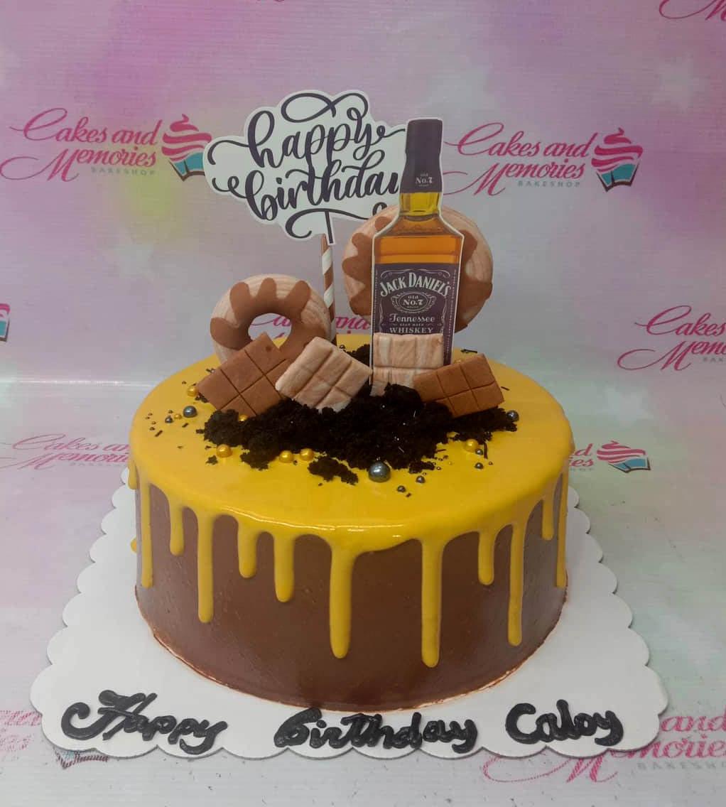 Chocolate drip cake with Jack Daniel's printout topper, chocolate bar decorations, and gold sprinkles on a brown base.
