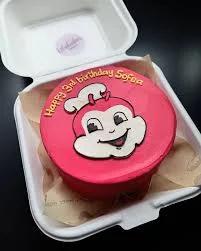 Pink Jollibee bento cake with a hand-piped Jollibee face and yellow birthday message in a white box.
