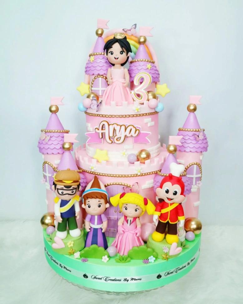 Pink three-tier castle cake with Jollibee characters, a princess topper, and a rainbow backdrop.