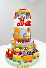 Three-tier light blue Jollitown theme cake with Jollibee character, rainbow, and colorful train figures.