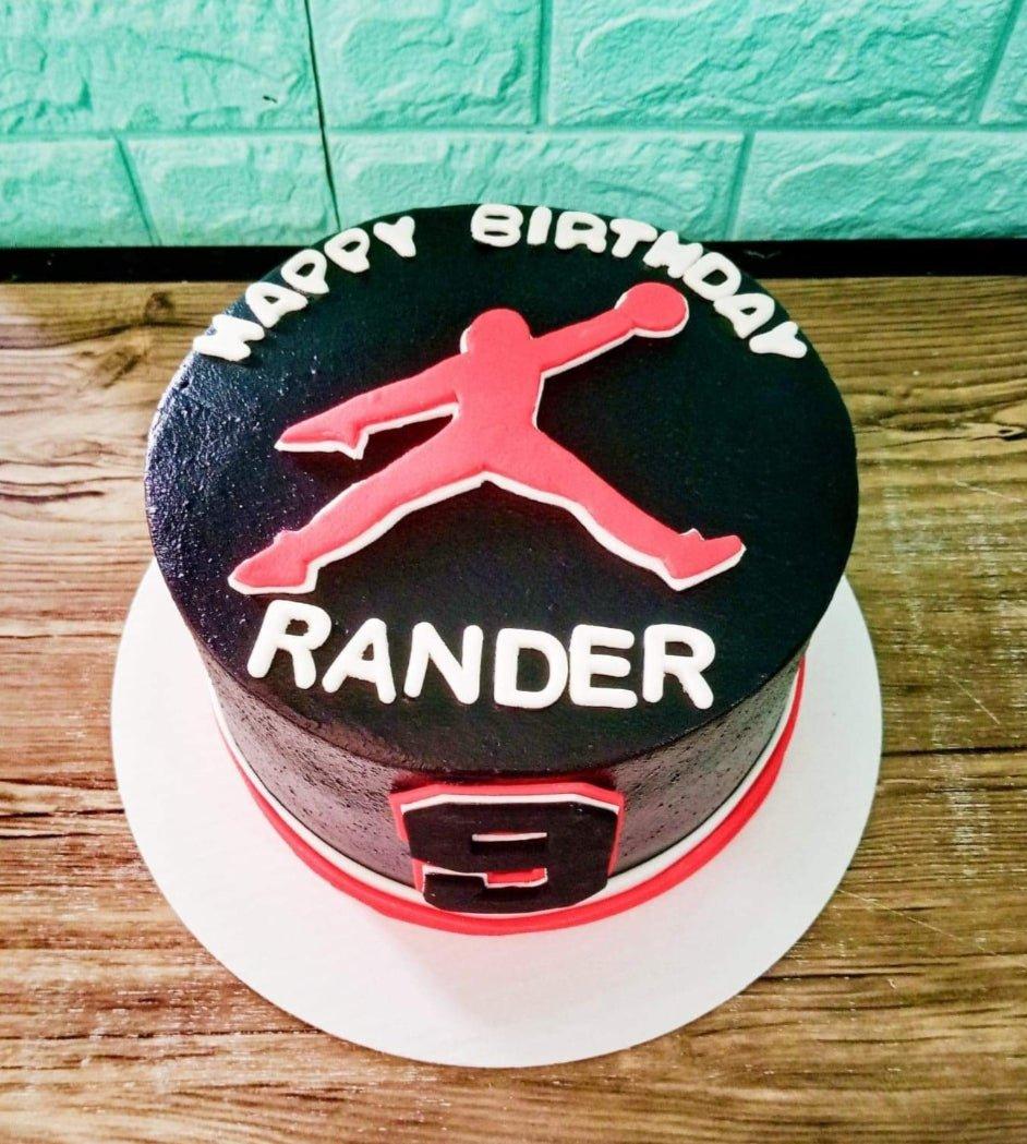 Black minimalist basketball themed cake with red Jordan logo and white icing text for Rander's 9th birthday.