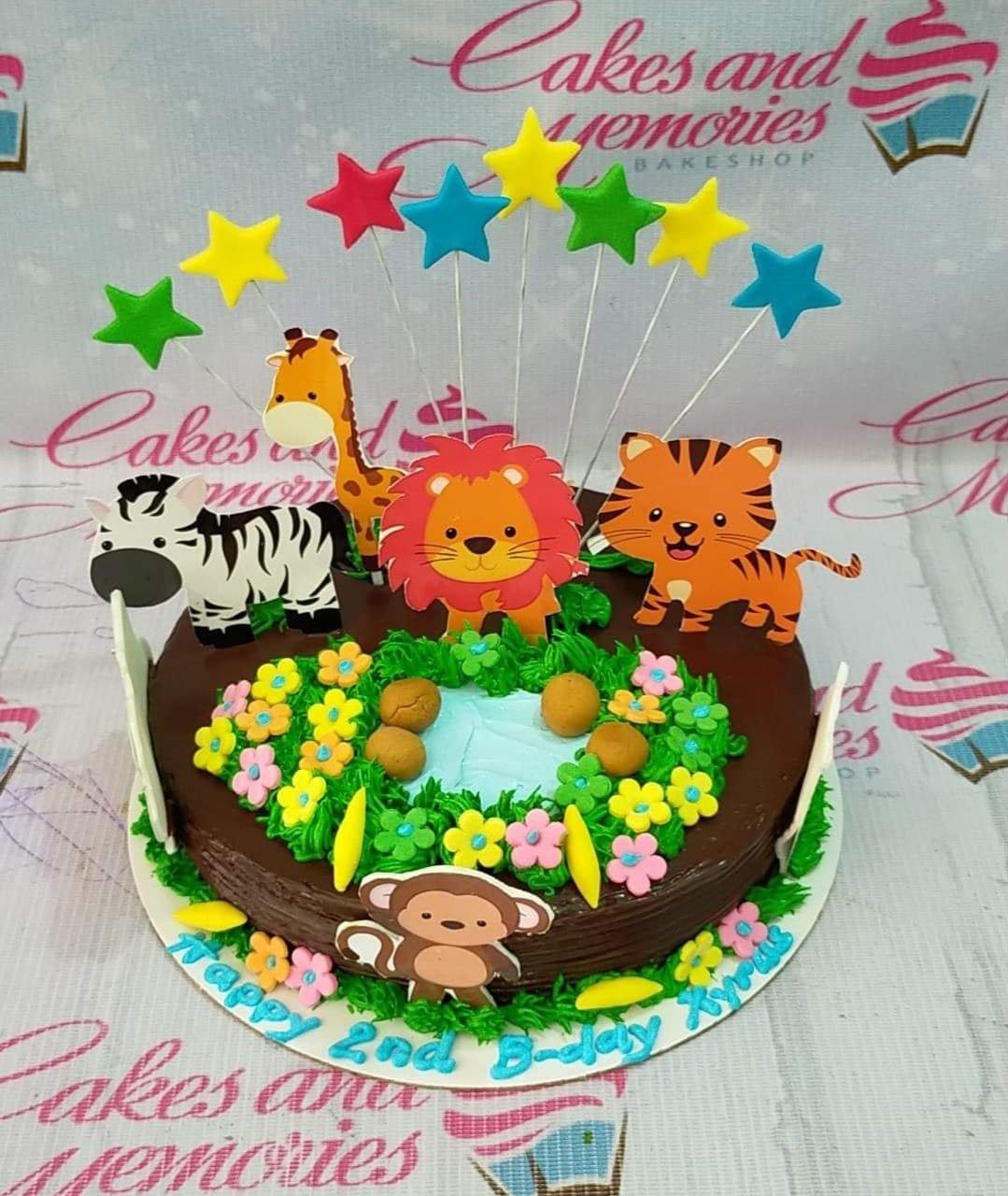 Chocolate jungle animal cake with lion, tiger, zebra, and giraffe toppers, green icing grass, and colorful stars.