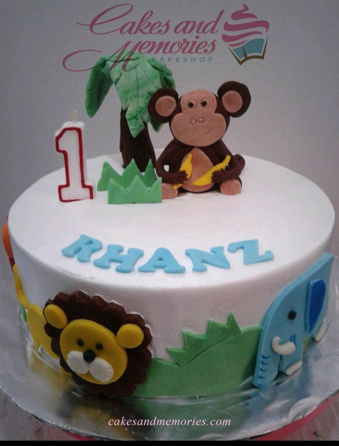 White 1-tier jungle themed birthday cake with a fondant monkey, elephant, lion, and palm tree decorations.