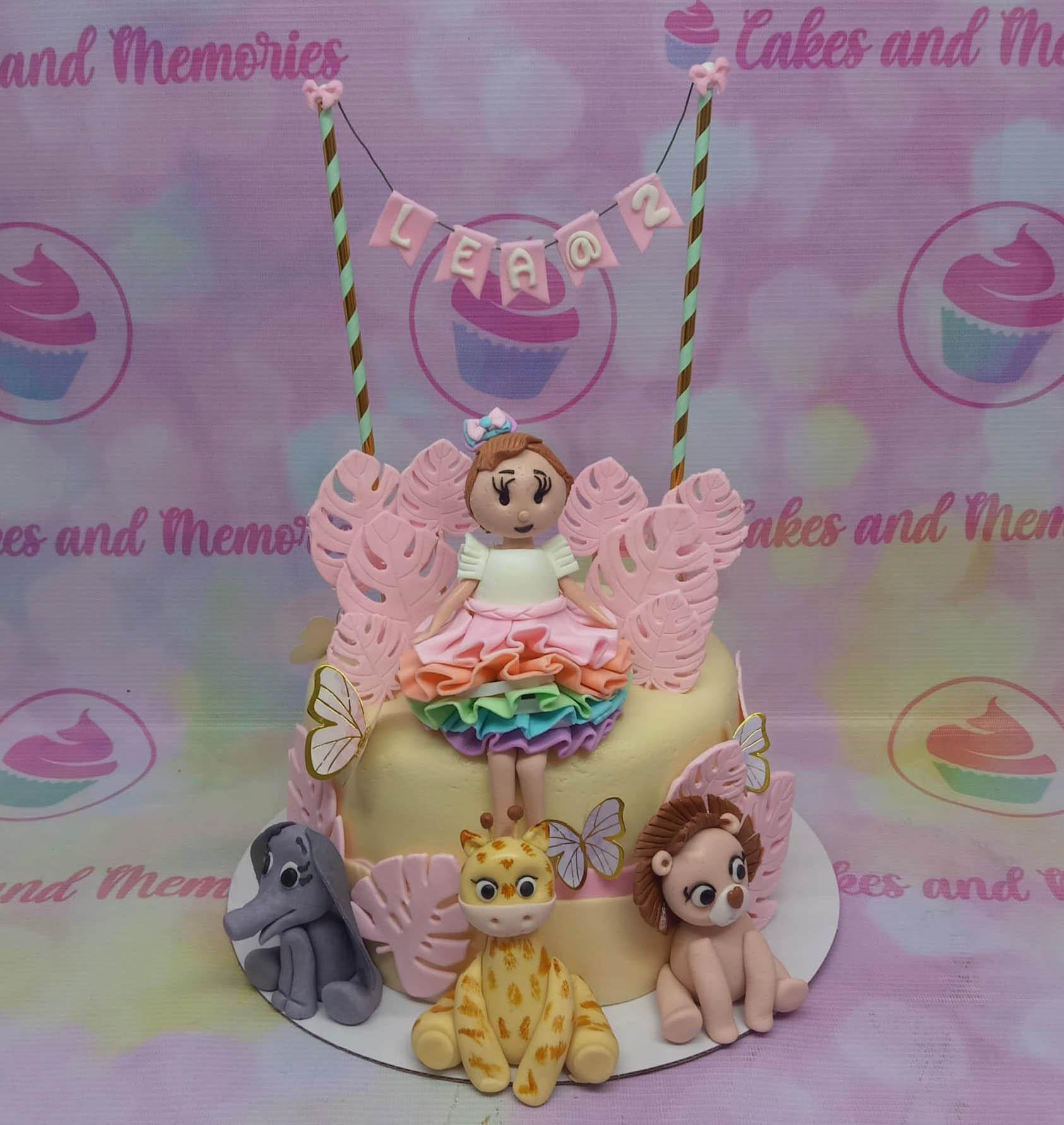 Yellow 1-tier jungle ballerina cake with fondant girl, lion, giraffe, and elephant figures and pink leaf accents.