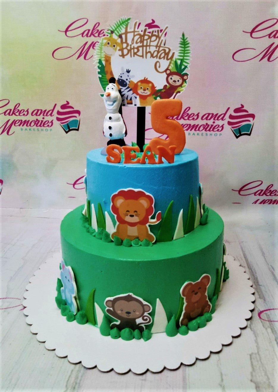 Two-tier jungle safari birthday cake with blue and green icing, featuring animal printouts and a fondant Olaf figure.