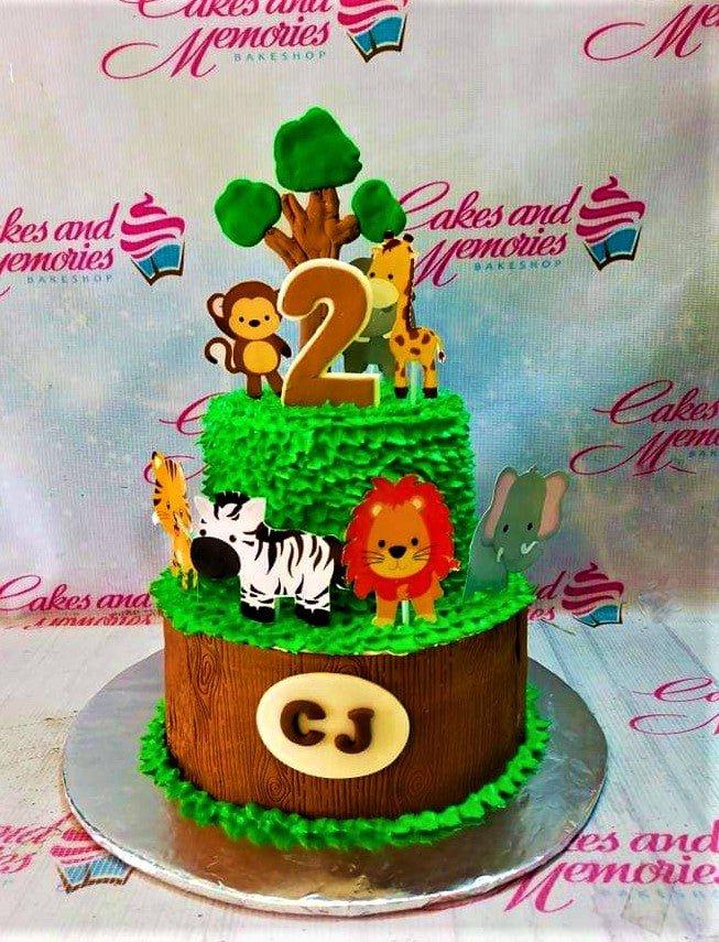 Two-tier jungle safari birthday cake with green grass icing, wood grain bottom tier, and animal printouts including a lion, zebra, and giraffe.