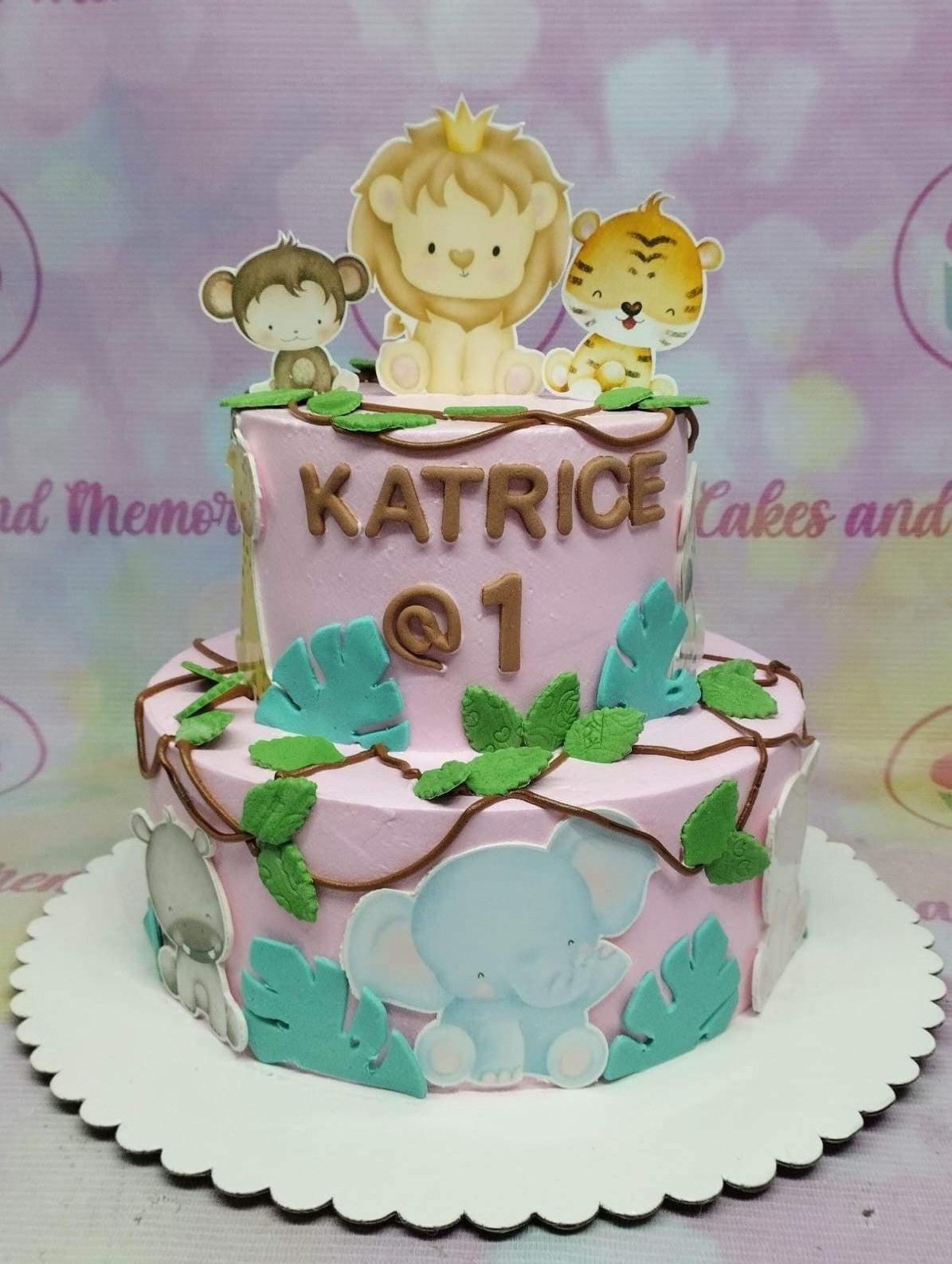Pink 2-tier jungle safari birthday cake with cute animal printouts, fondant leaves, and brown vines.