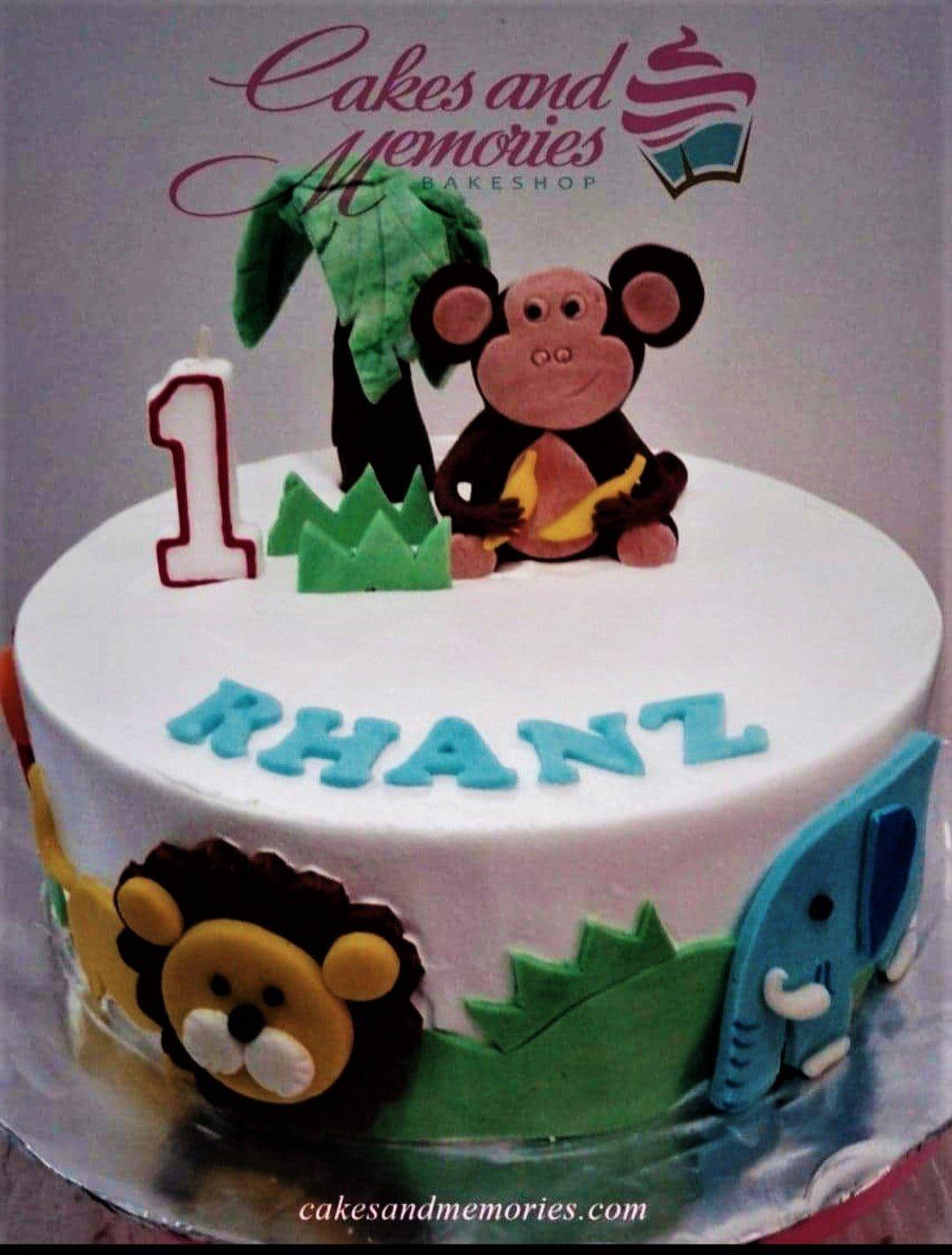 White 1-tier jungle safari birthday cake with a fondant monkey topper, lion and elephant side decorations, and a palm tree.
