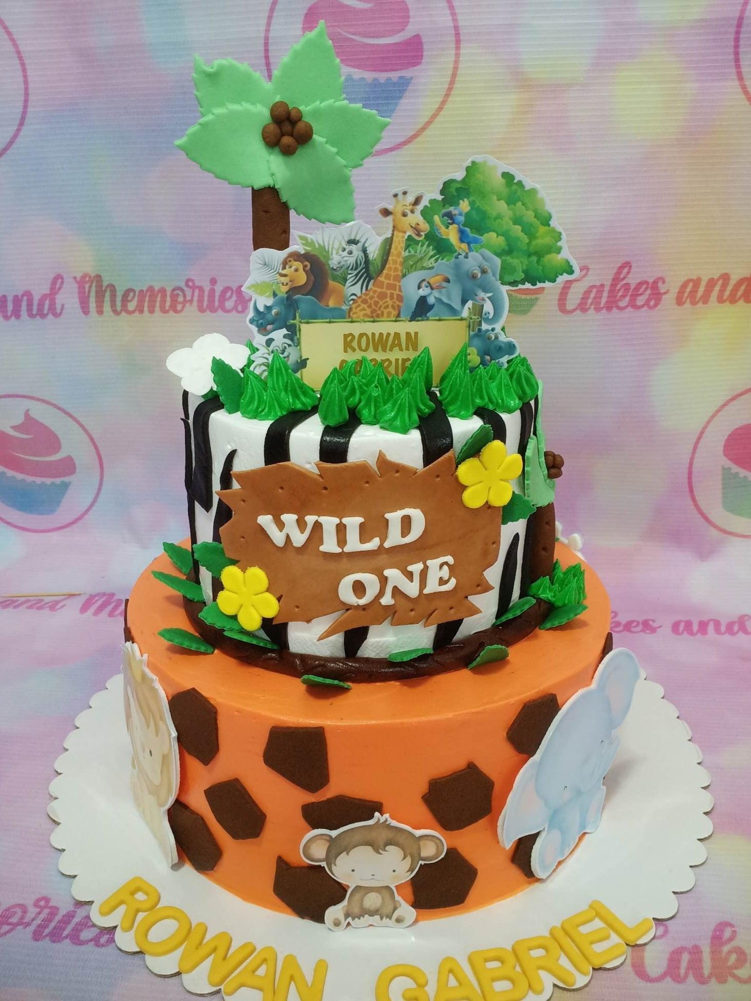 Two-tier jungle safari themed cake with orange giraffe print bottom and black and white zebra stripe top tier featuring animal toppers.