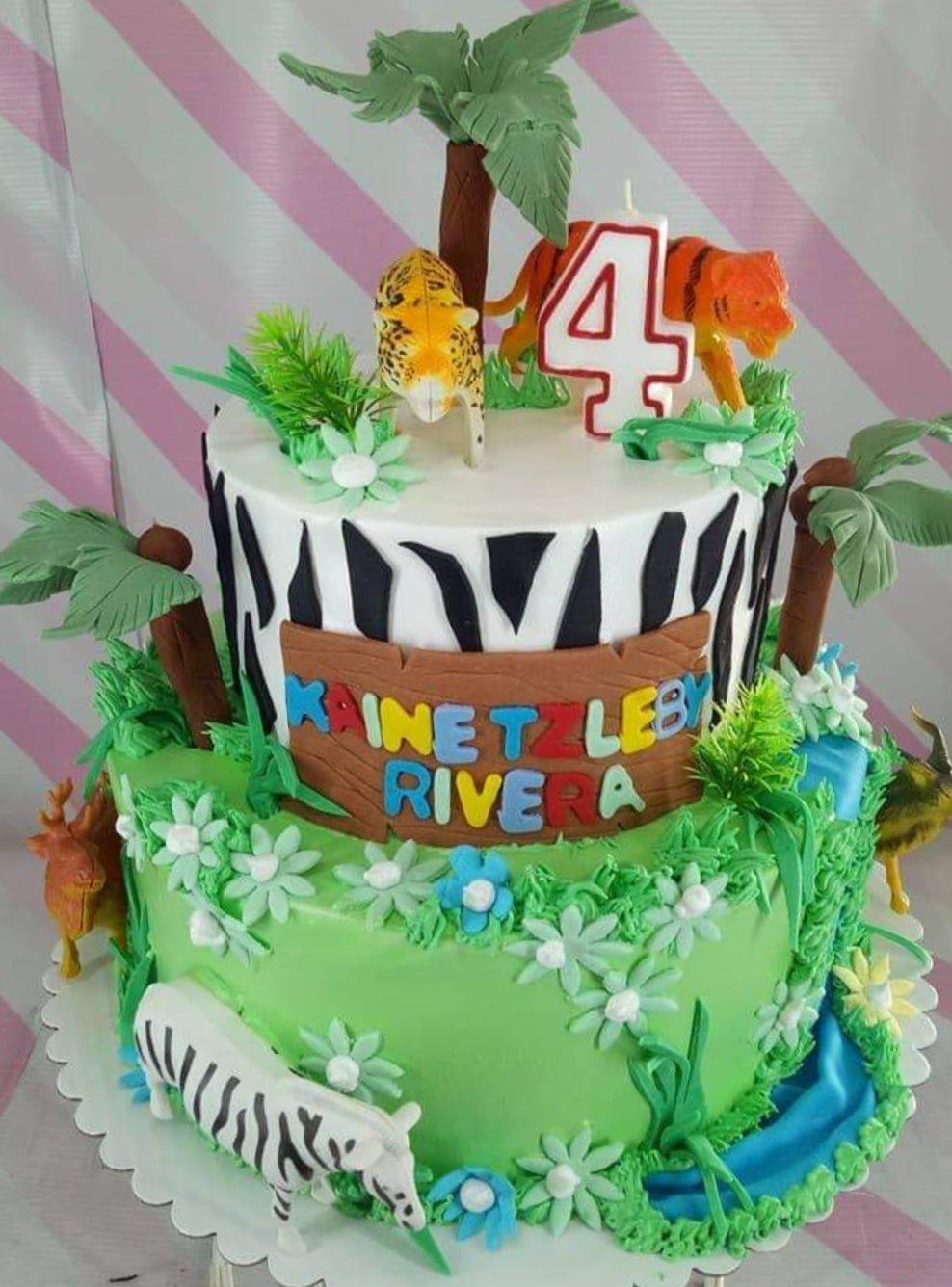 Two-tier jungle safari cake with zebra stripes, green grass icing, and plastic animal figures including a tiger, leopard, and zebra.