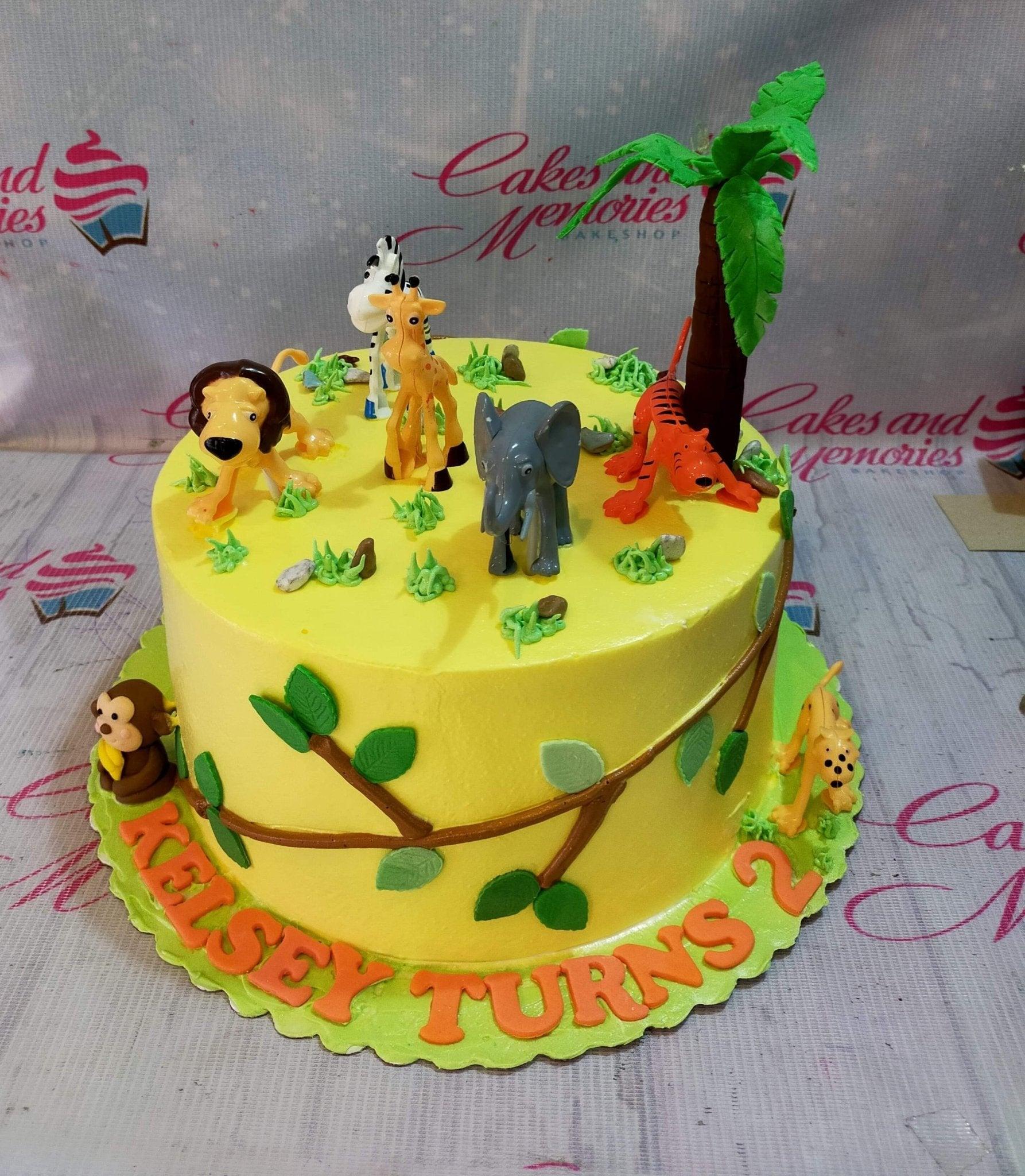 Yellow jungle safari birthday cake with 3D fondant animals including a lion, giraffe, elephant, tiger, and monkey with a palm tree.
