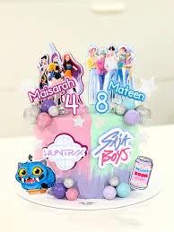 A colorful K-pop themed birthday cake with pink, mint, and purple icing, featuring character printouts and spherical decorations.