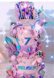 Three-tier pink and purple K-pop themed cake with character printouts, disco balls, and musical notes.