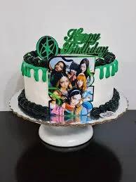 White and green K-pop themed birthday cake with a group photo printout and green icing drip.