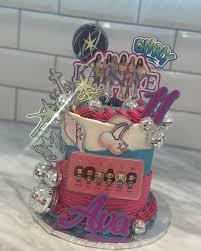 Pink and blue tiered cake with K-pop group printouts, disco balls, and a purple name topper for Ava.